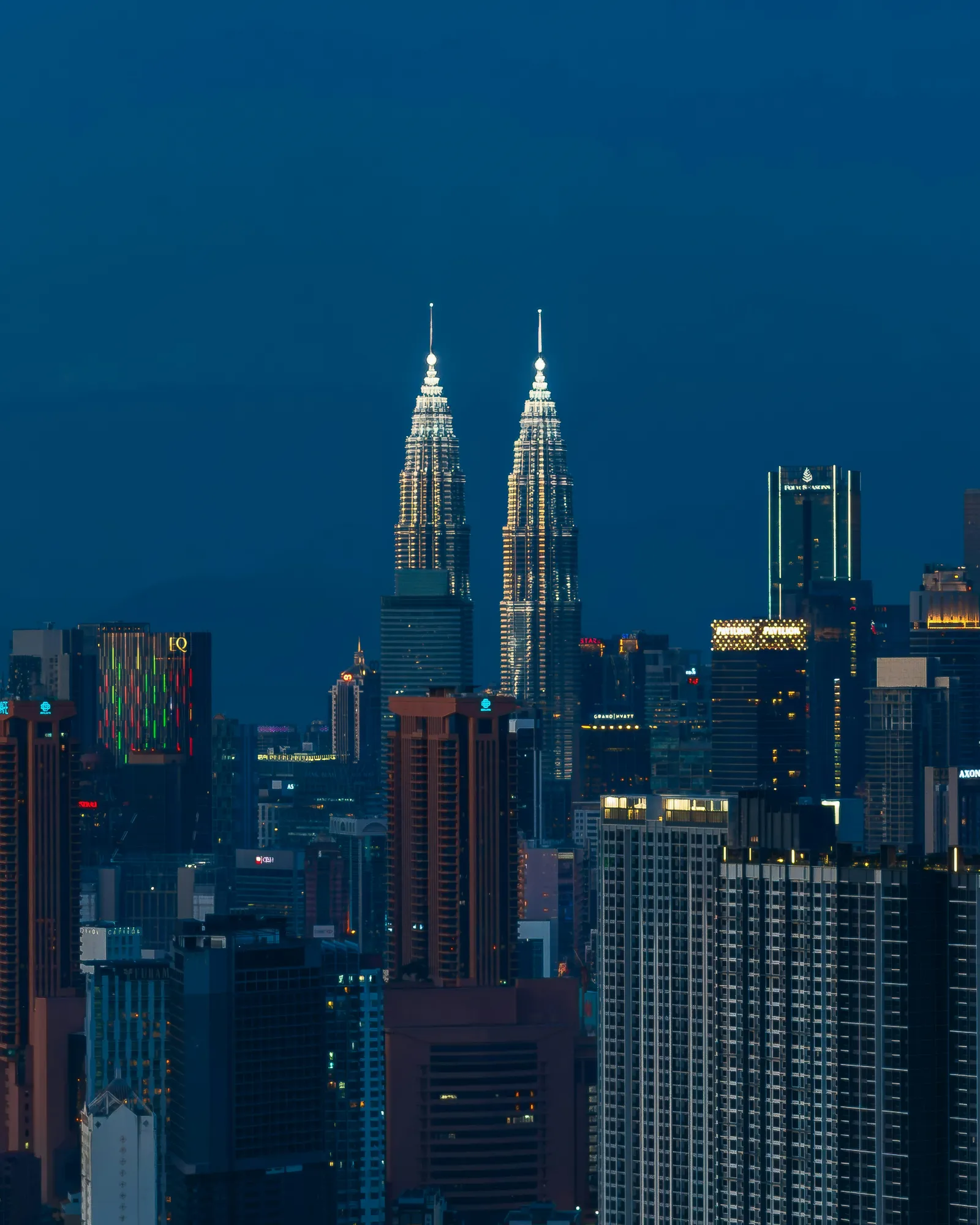 The Petronas Twin Towers lit up above the Kuala Lumpur skyline at dusk