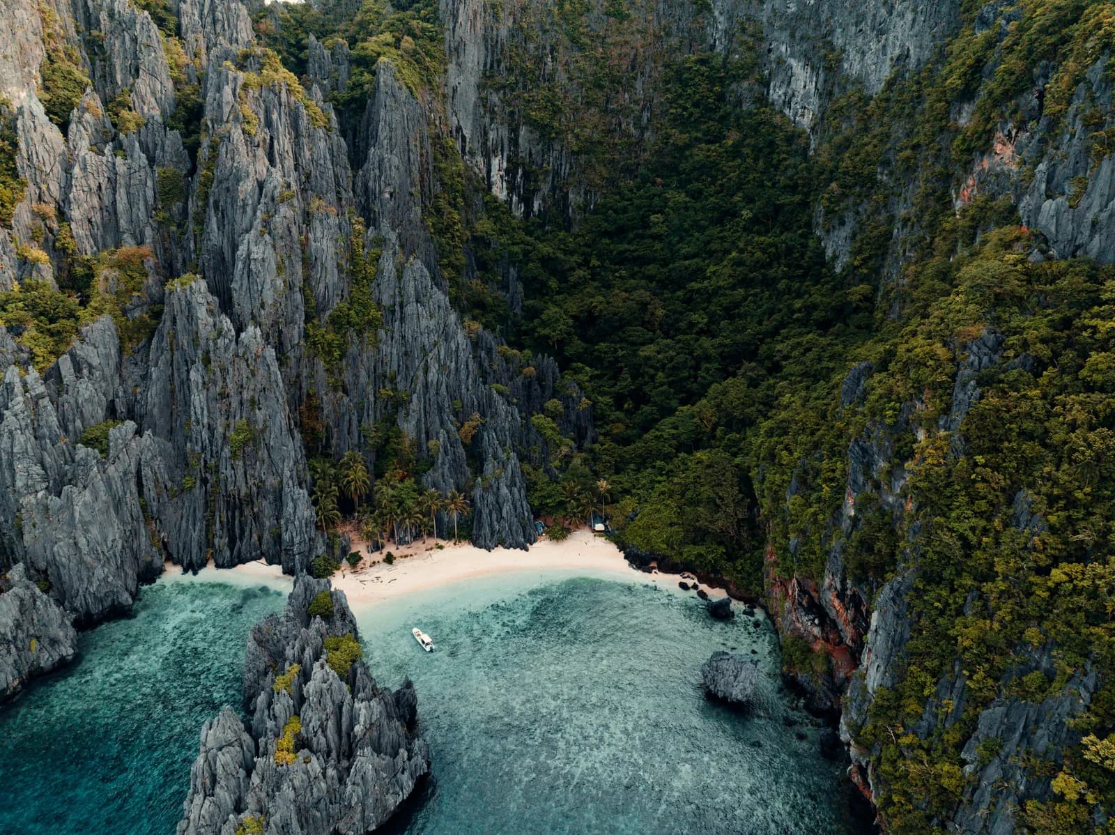 A white sand cove ringed by jungle-covered limestone cliffs in El Nido, Palawan