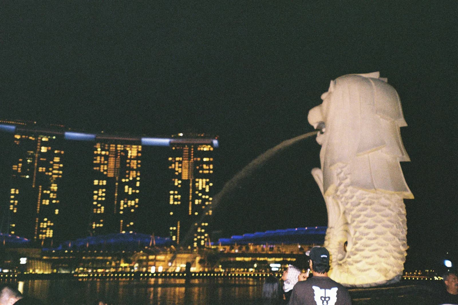 The Merlion statue spouting water into Marina Bay at night, with Marina Bay Sands lit up behind it